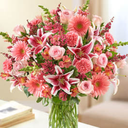 Tall pink mixed flower arrangement with lilies, roses, gerberas, and carnations in a clear glass vase