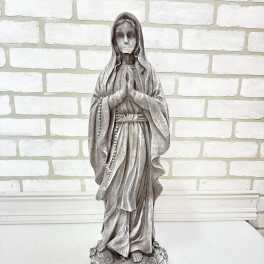 A gray religious statue of the Virgin Mary standing on a base