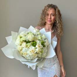 Woman holding a large bouquet of white roses and hydrangeas wrapped in white paper.