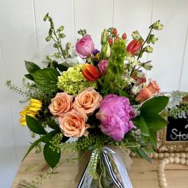 Mixed bouquet with peach roses, pink blooms, and tulips in a glass vase