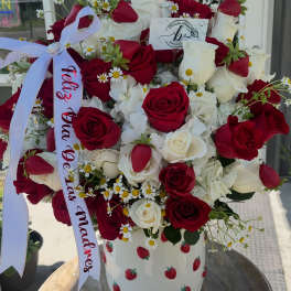 Bouquet of red and white roses in a strawberry-patterned vase with a ribbon