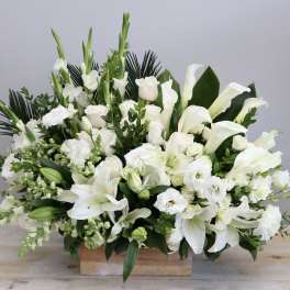 White floral arrangement with lilies, calla lilies, and roses in a wooden box