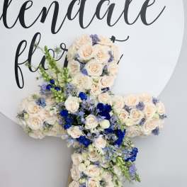 Large cross-shaped floral arrangement of cream roses with blue and lavender accents