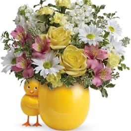 Yellow mug-shaped vase with mixed flowers and a small chick figurine
