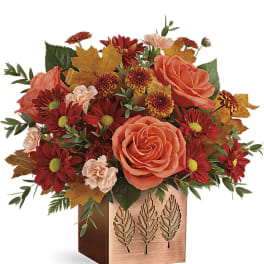 Orange roses and red mums in a copper cube vase with autumn leaves