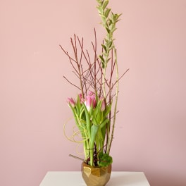 Tall arrangement of pink tulips in a gold vase