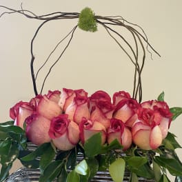 Pink roses arranged in a basket with curly branches arching above
