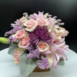 Pink roses and lilies arranged with purple blooms in a low vase