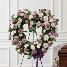 Lavender rose and white daisy funeral wreath on a stand with a purple ribbon