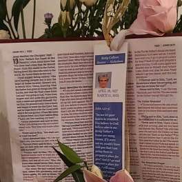 Floral memorial display with pink lilies, cream roses, and an open Bible