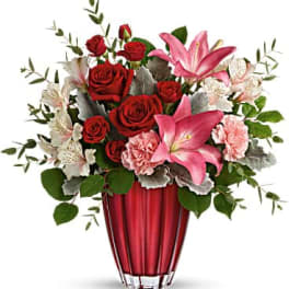 Red roses and pink lilies arranged in a red glass vase