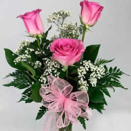 Pink roses in a clear glass vase with baby's breath and a pink ribbon bow