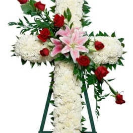 Tall white floral cross with red roses and pink lilies on a green easel stand
