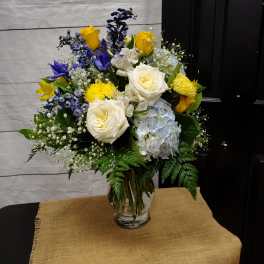 Mixed bouquet of white roses, yellow roses, blue flowers, and hydrangea in a glass vase