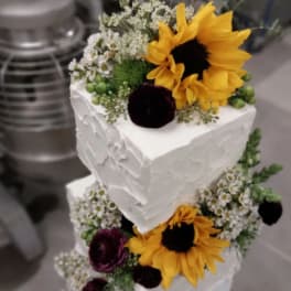 Two-tier white cake decorated with sunflowers and small white flowers