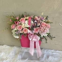 Pink and white flower arrangement in a bright pink handbag-style container with ribbon