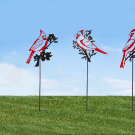 Three red cardinal yard stakes on metal stands in a grassy field