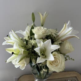 White lilies and roses arranged in a clear glass vase