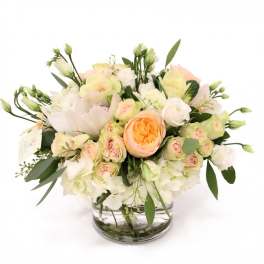 Round arrangement of white and peach roses and hydrangeas in a clear glass vase