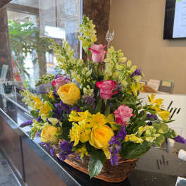 Basket arrangement with yellow and pink roses, yellow alstroemeria, snapdragons, and purple accents