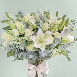 White lilies and roses in a glass vase with a pale ribbon