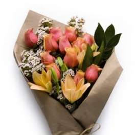 Wrapped bouquet of pink roses and peach lilies with small white filler flowers in kraft paper