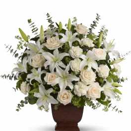 Large white lily, rose, and carnation arrangement in a brown urn with eucalyptus accents