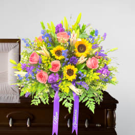Bright casket spray with sunflowers, pink roses, lilies and purple blooms on a wooden casket