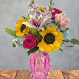 Mixed bouquet with sunflowers, lilies, roses, and hydrangeas in a pink vase