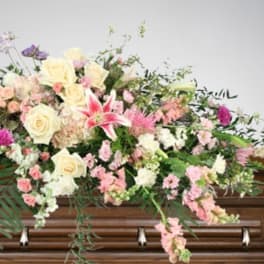 Pastel floral spray on a wooden casket with roses and lilies