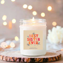 Lit scented candle in a glass jar with a "Best Sister Ever" label