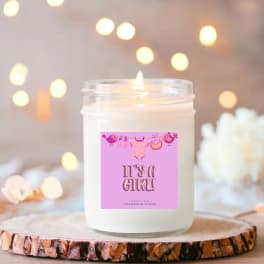 White jar candle with a pink "It's a Girl!" label