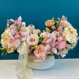 Pastel floral arrangement with orchids and roses in a low white vase