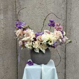 Purple and white floral arrangement in a gray vase on a draped pedestal