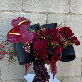 Deep red floral arrangement with anthuriums and roses in a white pedestal vase