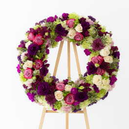 Circular floral wreath on a wooden easel with pink, purple, and cream blooms