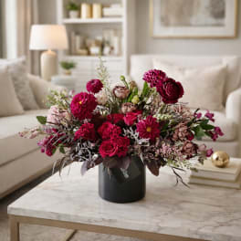 Pink and burgundy flower arrangement in a black vase on a coffee table