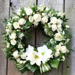 White rose and lily wreath with green foliage on a wooden background