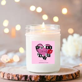 Lit white candle in a glass jar with a pink label