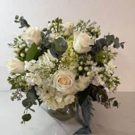 White rose bouquet in a clear glass vase with eucalyptus and small white filler flowers