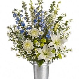 White lilies and blue flowers arranged in a silver bucket