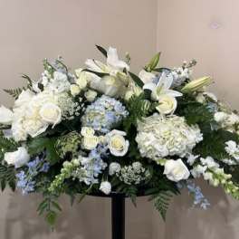 Large white floral arrangement with lilies, roses, and hydrangeas on a stand