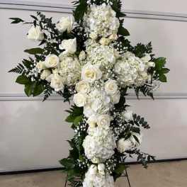 White floral cross arrangement with roses and hydrangeas on a stand
