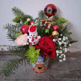 Christmas arrangement with red roses, a snowman ornament, and festive baubles in a decorated tin