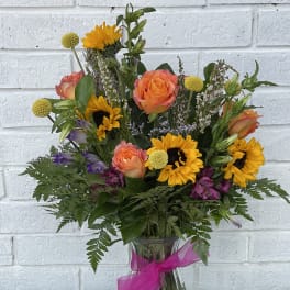Bouquet of sunflowers, orange roses, and purple flowers in a glass vase