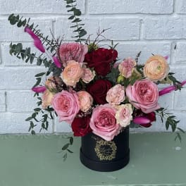 Pink and red roses arranged in a black hatbox with eucalyptus