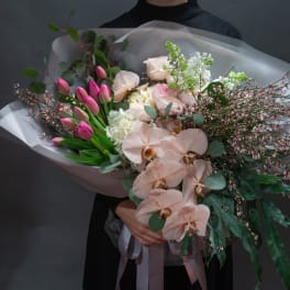 Bouquet of pink tulips, pale roses, and peach orchids wrapped in translucent paper