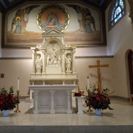 Two red floral arrangements flank a church altar with statues and a crucifix.