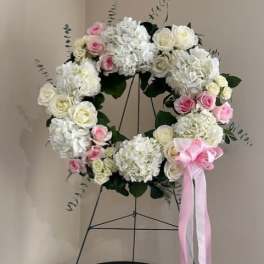 White and pink floral wreath on a stand with a pink ribbon