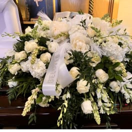 Large white funeral casket spray of roses and mixed blooms with ribbon on a dark wood casket